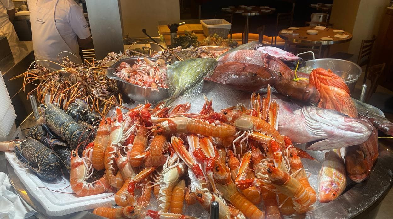 Expositor de Los Marinos José con cigalas, langostas, bogavantes y pescado de roca sobre hielo, con las mesas de la sala al fondo